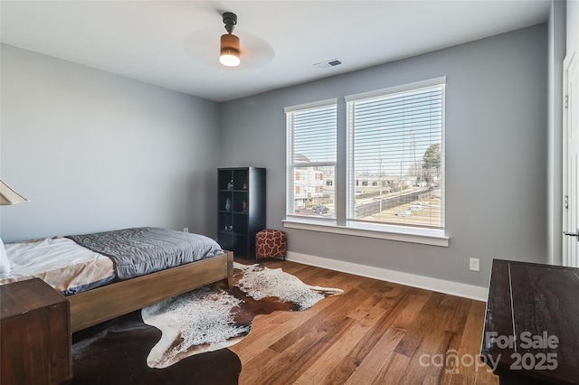 bedroom featuring ceiling fan, wood finished floors, visible vents, and baseboards