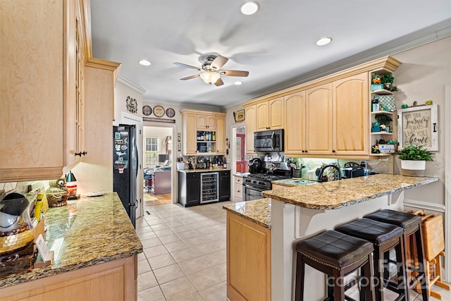 kitchen with stainless steel gas range oven, wine cooler, a breakfast bar area, freestanding refrigerator, and light brown cabinetry