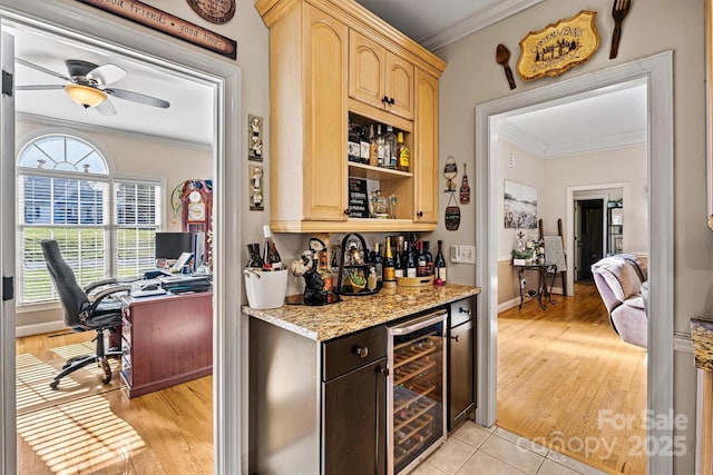 bar with beverage cooler, a ceiling fan, light wood-style floors, a bar, and crown molding