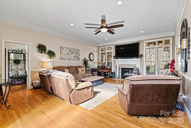 living room with light wood-style floors, ceiling fan, ornamental molding, and a glass covered fireplace