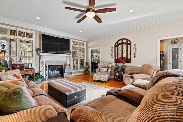 living room with ceiling fan, recessed lighting, wood finished floors, a glass covered fireplace, and crown molding