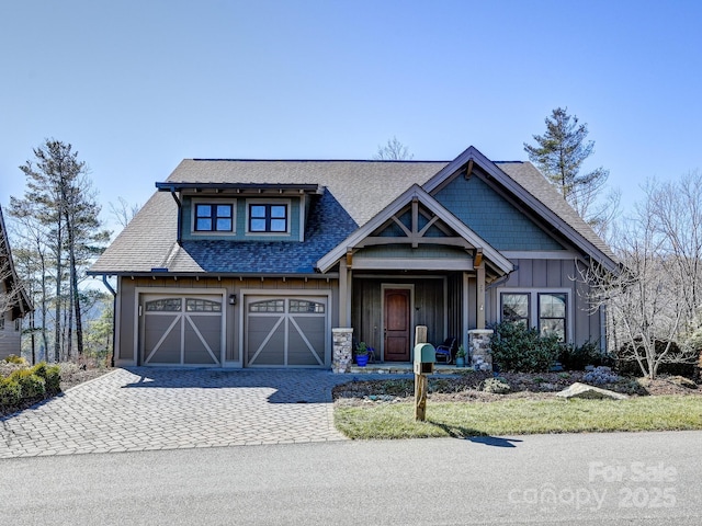 craftsman-style house with an attached garage, decorative driveway, board and batten siding, and roof with shingles