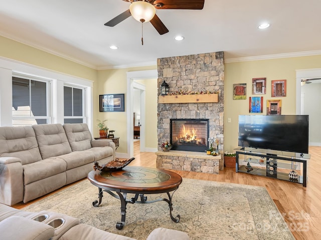 living area with a ceiling fan, ornamental molding, wood finished floors, a stone fireplace, and recessed lighting