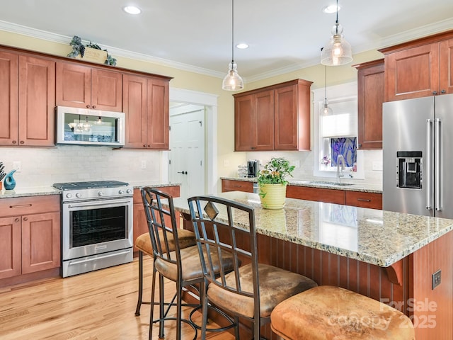 kitchen with appliances with stainless steel finishes, crown molding, light wood-type flooring, pendant lighting, and a sink