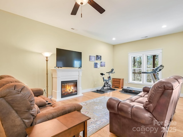 living room featuring recessed lighting, light wood-type flooring, a glass covered fireplace, and baseboards