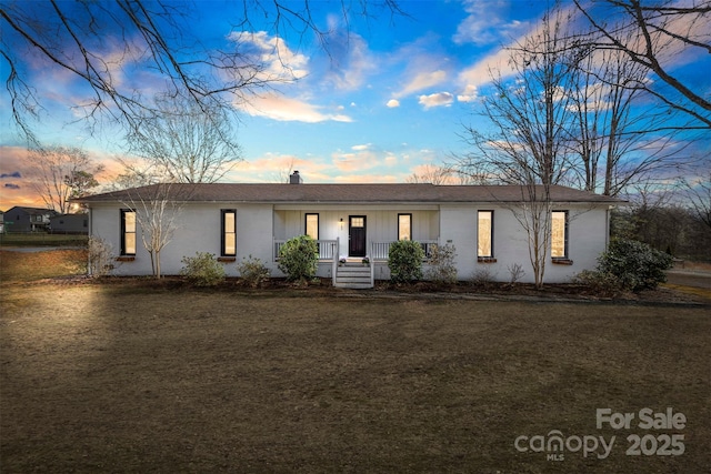 ranch-style house with covered porch, a chimney, and a lawn