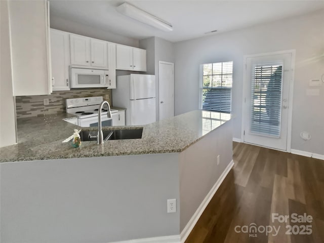 kitchen with a peninsula, white appliances, light stone counters, and white cabinets