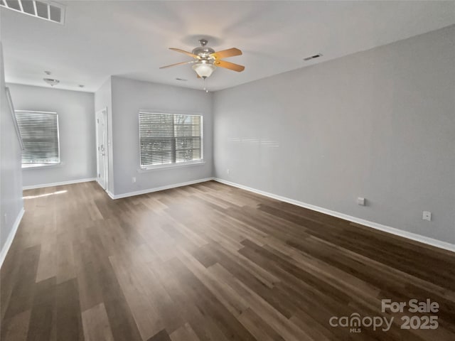 empty room featuring dark wood-style floors, ceiling fan, visible vents, and baseboards