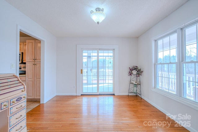 doorway featuring light wood-type flooring, a textured ceiling, and baseboards