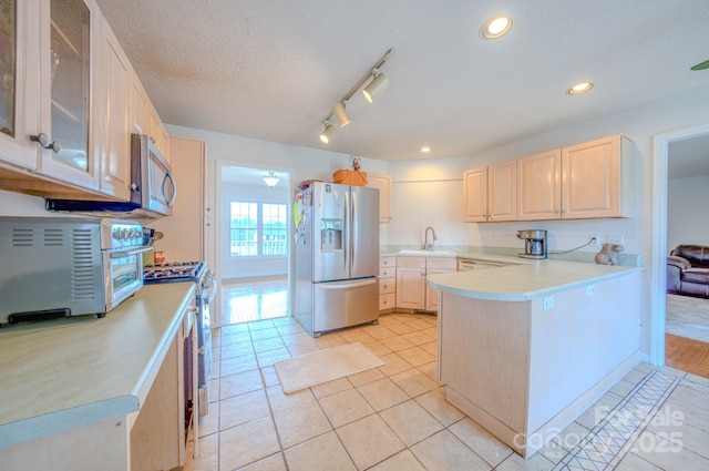 kitchen featuring a peninsula, light countertops, stainless steel appliances, light brown cabinetry, and a sink