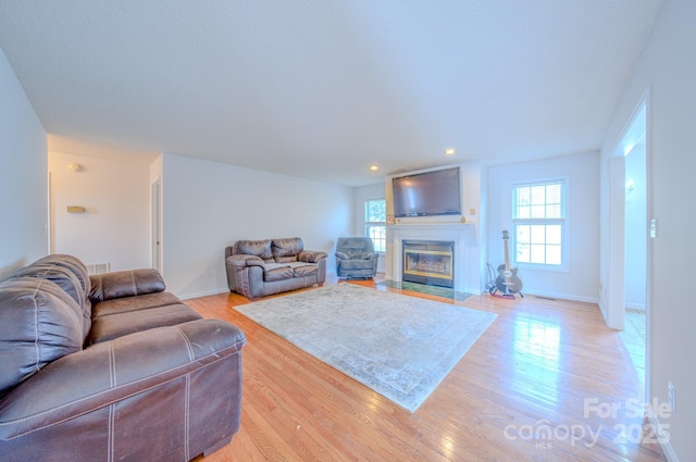 living area with light wood-type flooring, a fireplace with flush hearth, baseboards, and recessed lighting