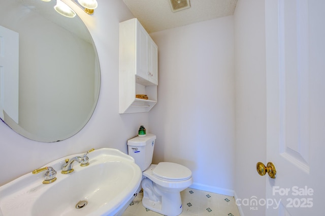 half bathroom featuring toilet, a sink, visible vents, and baseboards