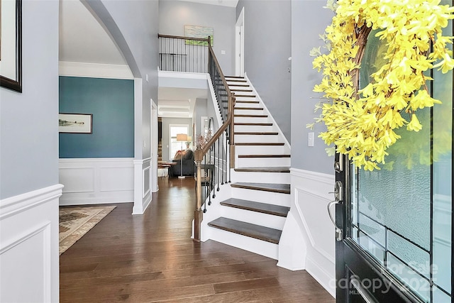 entryway with dark wood-style floors, ornamental molding, a wainscoted wall, and stairs