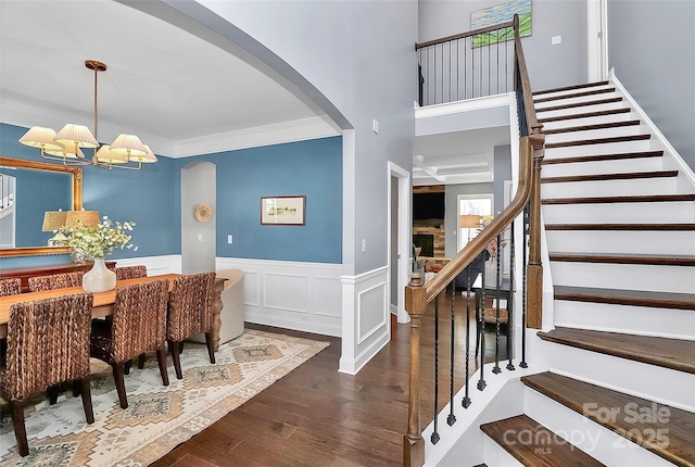 interior space with arched walkways, dark wood finished floors, a notable chandelier, stairway, and wainscoting