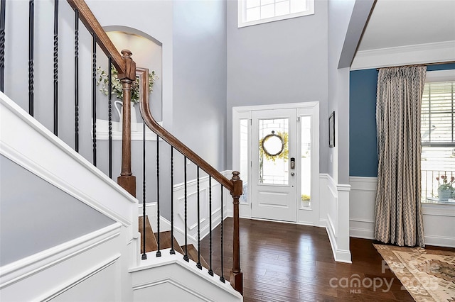 foyer entrance with a wainscoted wall, stairway, ornamental molding, dark wood-style flooring, and a decorative wall