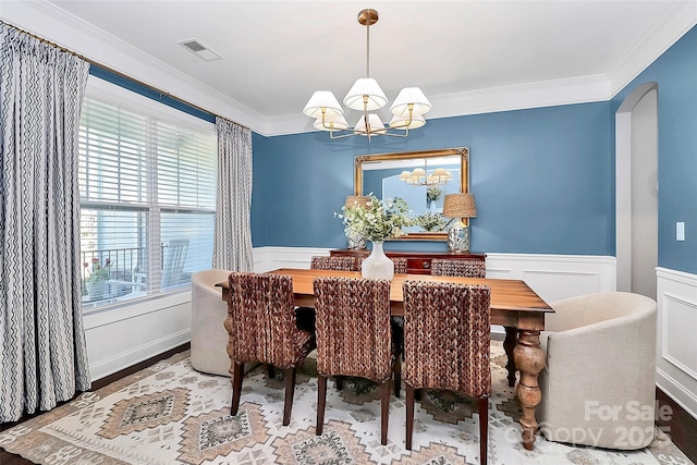 dining space featuring ornamental molding, arched walkways, a wainscoted wall, and a notable chandelier