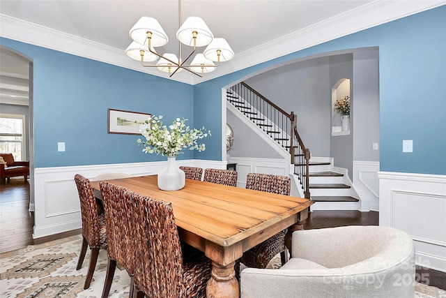 dining space with arched walkways, a wainscoted wall, stairs, and a chandelier