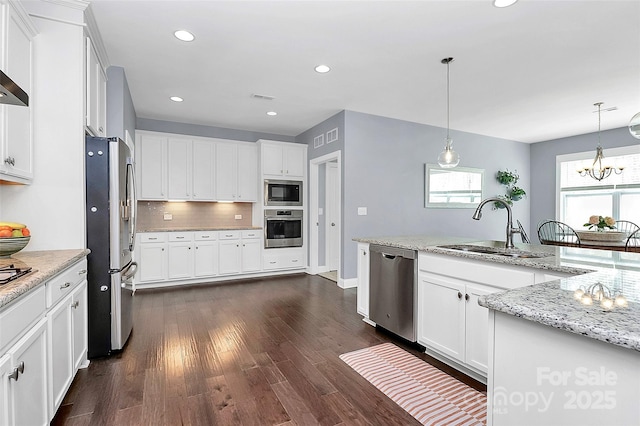 kitchen featuring pendant lighting, appliances with stainless steel finishes, white cabinetry, a sink, and light stone countertops