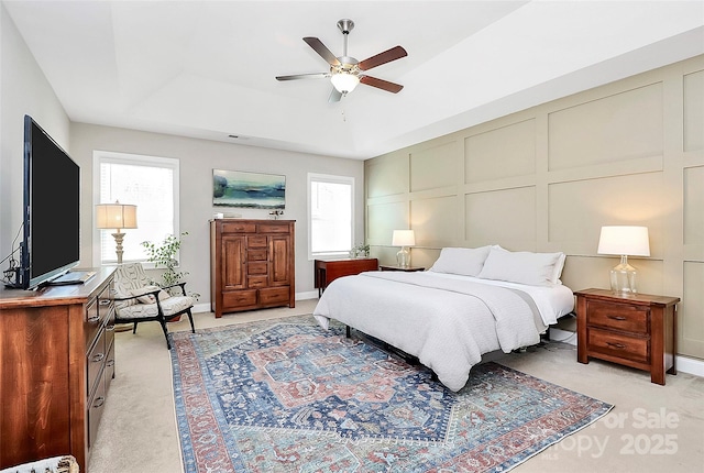 bedroom featuring light carpet, a tray ceiling, multiple windows, and a decorative wall