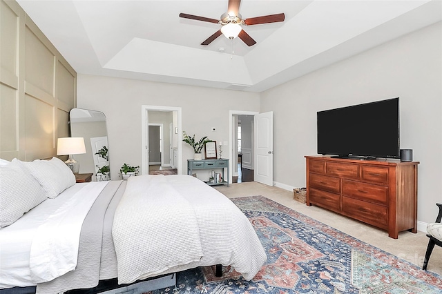 bedroom with baseboards, a raised ceiling, a ceiling fan, and light colored carpet