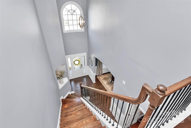 staircase with a towering ceiling, a chandelier, and wood finished floors