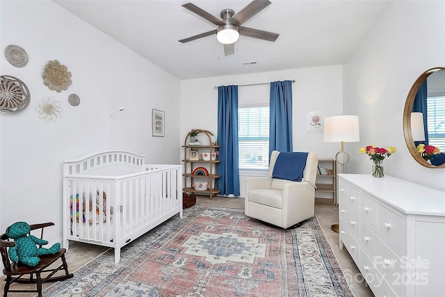 bedroom with a nursery area, visible vents, and a ceiling fan