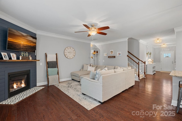 living area featuring dark wood-style floors, stairway, ornamental molding, and a glass covered fireplace