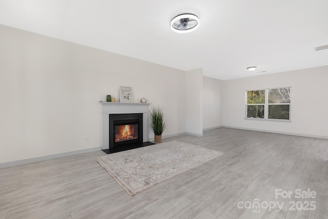 unfurnished living room featuring light wood finished floors, a fireplace with flush hearth, and baseboards