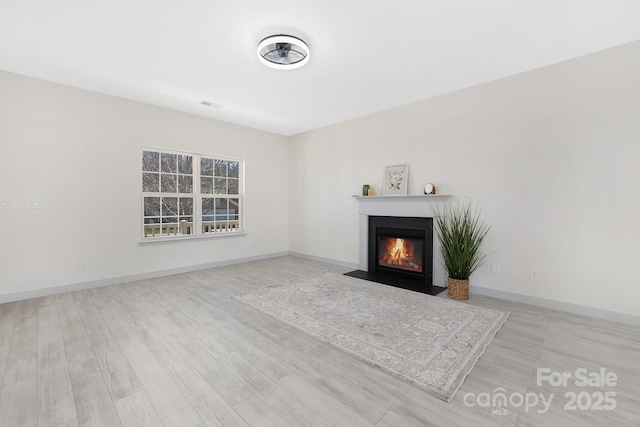 unfurnished living room with light wood-style floors, a fireplace with flush hearth, and baseboards