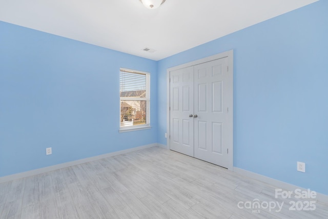 unfurnished bedroom with baseboards, visible vents, light wood-style flooring, and a closet