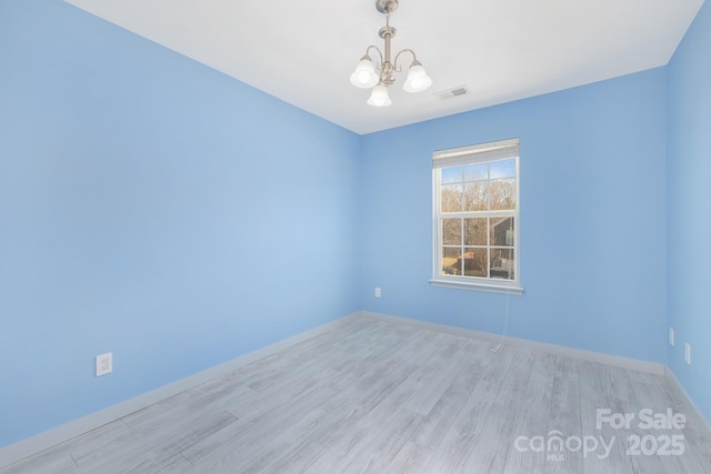 empty room featuring baseboards, wood finished floors, visible vents, and an inviting chandelier