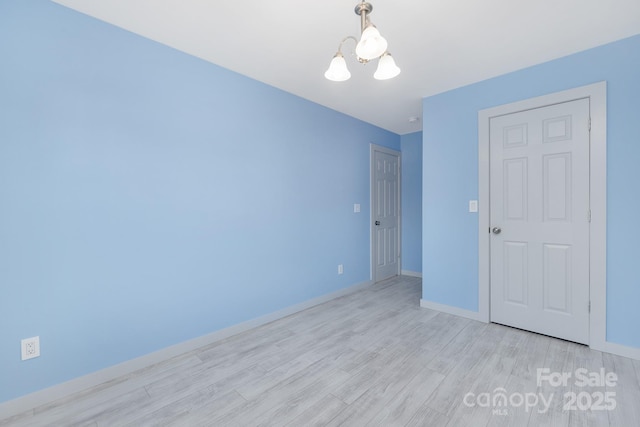 empty room with light wood-style floors, baseboards, and an inviting chandelier