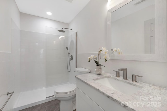 bathroom featuring visible vents, toilet, vanity, a walk in shower, and tile walls