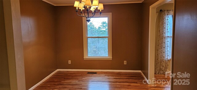 spare room featuring an inviting chandelier, crown molding, baseboards, and wood finished floors