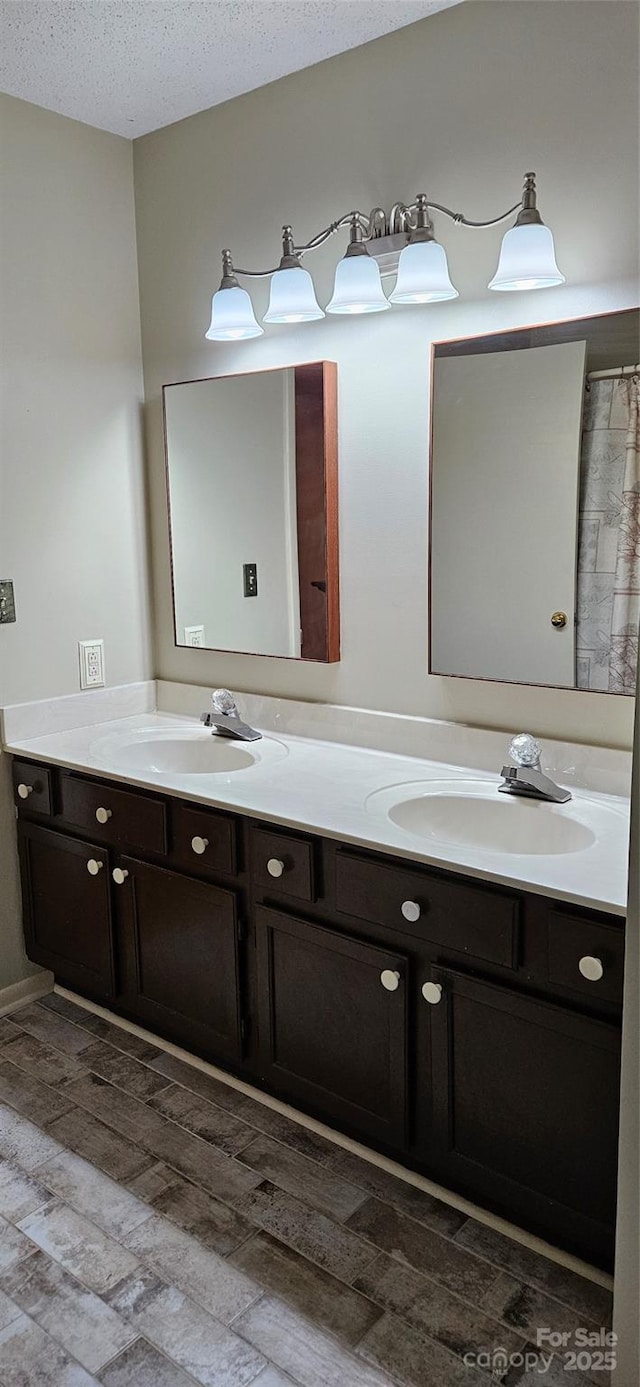 full bathroom featuring double vanity, wood finished floors, a sink, and a textured ceiling