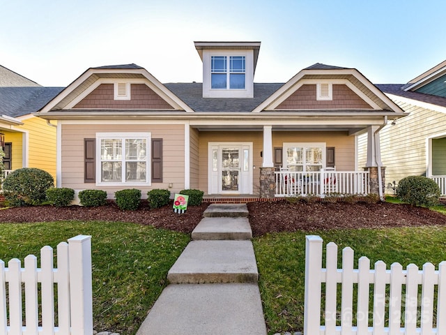 craftsman-style house featuring covered porch, fence, and a front lawn