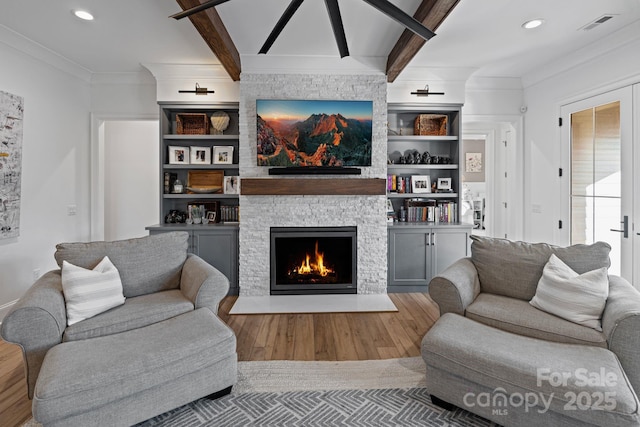 living area featuring a fireplace, wood finished floors, visible vents, ornamental molding, and beam ceiling