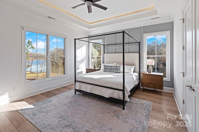 bedroom with baseboards, visible vents, wood finished floors, a tray ceiling, and crown molding