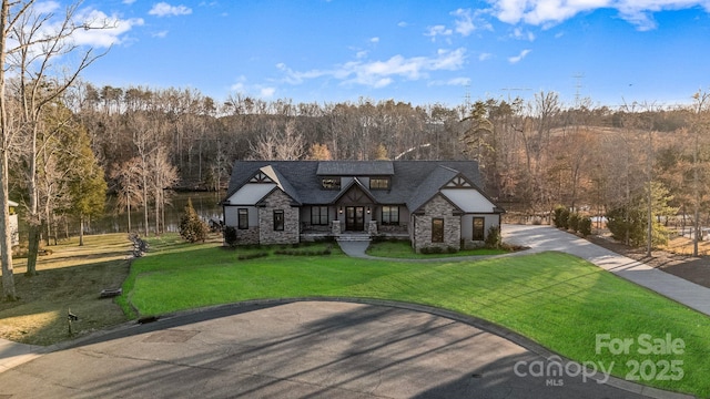 view of front facade with stone siding, a front lawn, and a view of trees