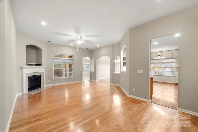 unfurnished living room featuring light wood-style floors, a fireplace, baseboards, and a ceiling fan