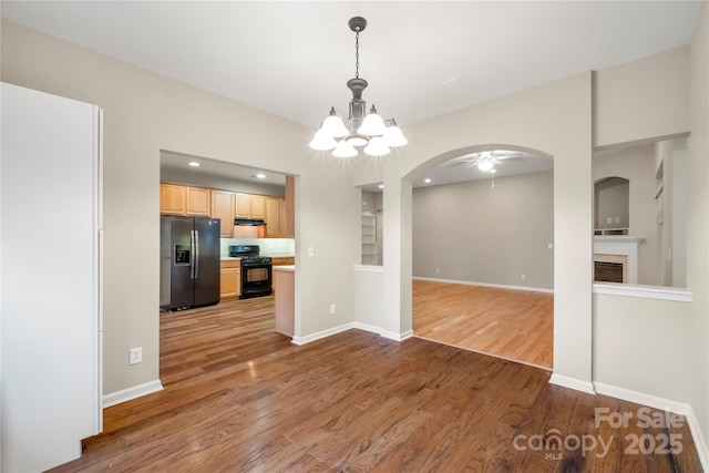 interior space with arched walkways, a fireplace, baseboards, and wood finished floors