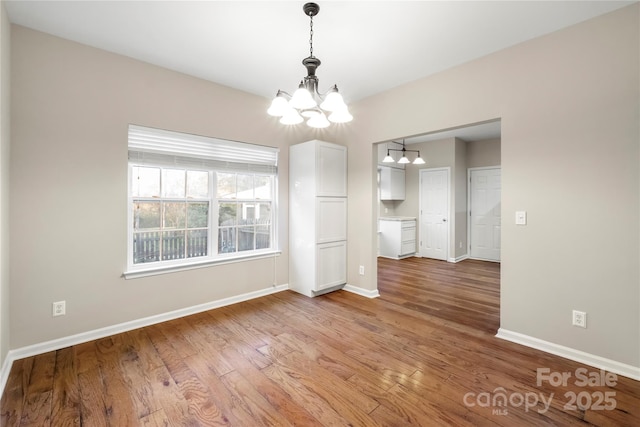 unfurnished dining area featuring baseboards, a chandelier, and wood finished floors