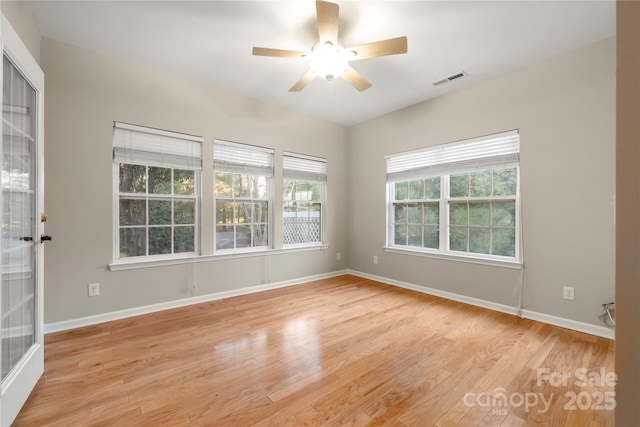 spare room featuring light wood-type flooring, baseboards, visible vents, and a wealth of natural light