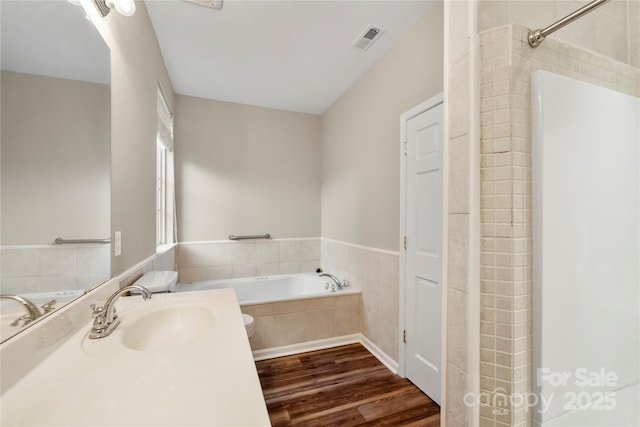 bathroom featuring a relaxing tiled tub, visible vents, wood finished floors, and vanity