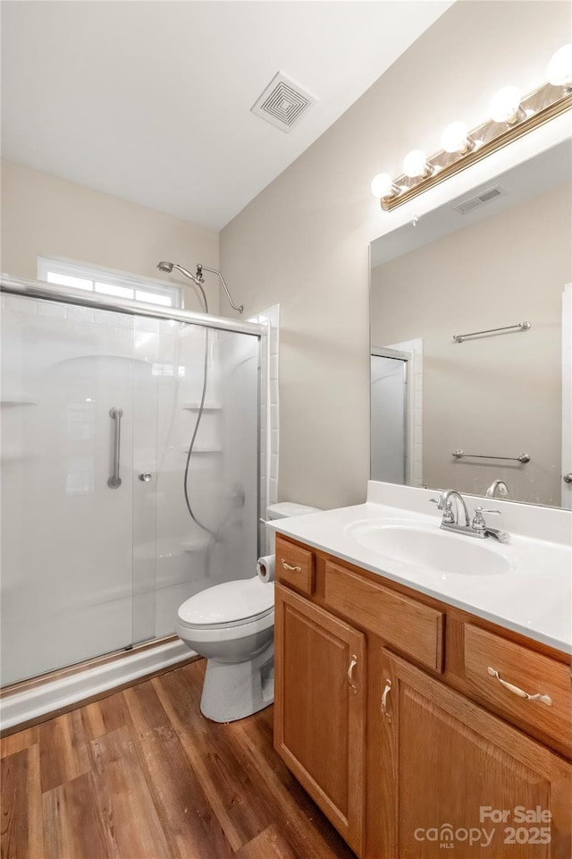 bathroom with toilet, wood finished floors, vanity, visible vents, and a stall shower