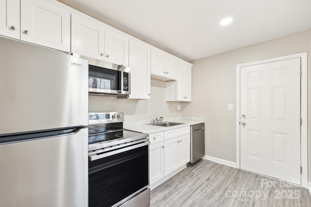 kitchen featuring light wood-style floors, appliances with stainless steel finishes, white cabinets, and a sink