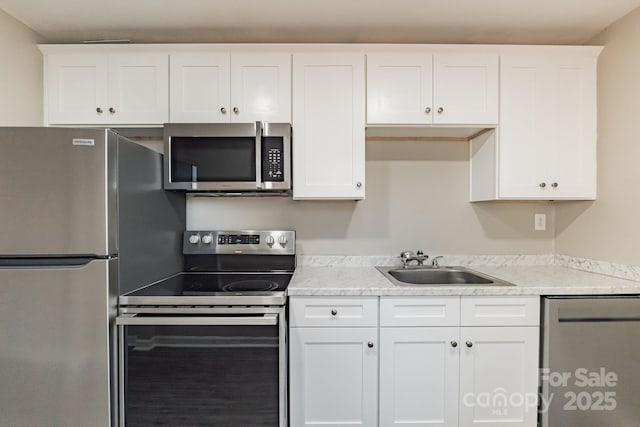 kitchen with stainless steel appliances, white cabinets, a sink, and light stone counters