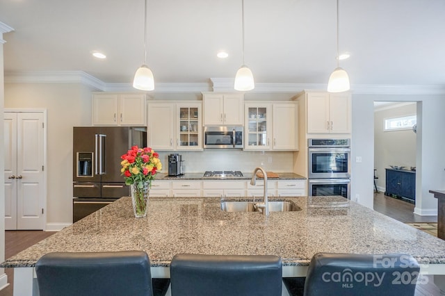 kitchen with light stone counters, glass insert cabinets, hanging light fixtures, stainless steel appliances, and a sink