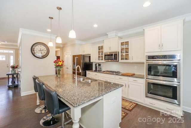 kitchen with appliances with stainless steel finishes, glass insert cabinets, a breakfast bar, a kitchen island with sink, and a sink