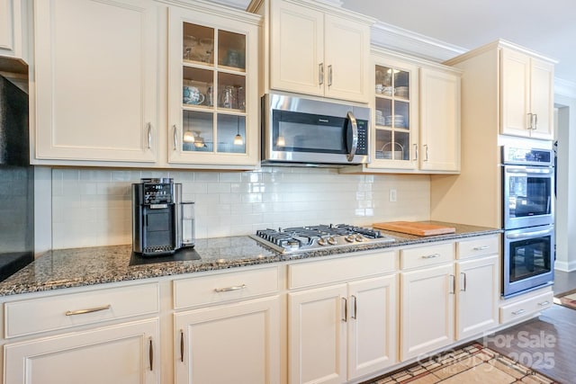 kitchen featuring appliances with stainless steel finishes, dark stone counters, glass insert cabinets, and backsplash